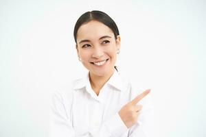 Successful korean businesswoman, pointing finger right, showing advertisement on banner, standing over white background photo