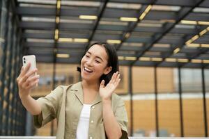 Happy girl says hi to camera on smartphone, video call while stands on street photo