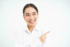 Successful korean businesswoman, pointing finger right, showing advertisement on banner, standing over white background photo