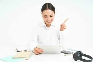 Portrait of successful female employee, asian woman talks via digital tablet on video chat, has online meeting with client while sits in her office, white background photo