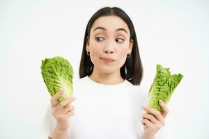 Healthy diet and organic food. Smiling asian woman showing cabbage, eating lettuce, cleansing her body, on detox, white background photo