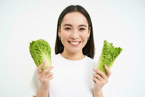 sano dieta y orgánico alimento. sonriente asiático mujer demostración repollo, comiendo lechuga, limpieza su cuerpo, en desintoxicación, blanco antecedentes foto