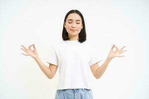 Peaceful smiling asian woman, standing calm and relaxed, holds hands in zen, meditation pose, isolated over white background photo