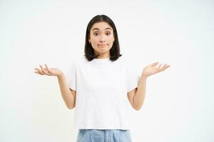 Portrait of confused korean woman, shrugging shoulders, looks puzzled, dont know, has no idea, stands over white background photo