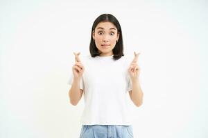 Portrait of young asian woman, looking hopeful, cross arms on chest, praying for smth, anticipating, making wish, isolated on white background photo