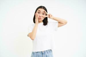 positivo coreano chica, muestra paz, signo v y besos rostro, posando linda en contra blanco antecedentes foto