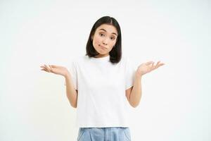 Portrait of confused korean woman, shrugging shoulders, looks puzzled, dont know, has no idea, stands over white background photo