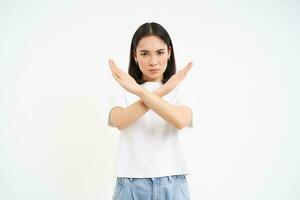 Young serious woman shows stop sign, rejects smth, disapprove and ban action, stands over white background photo