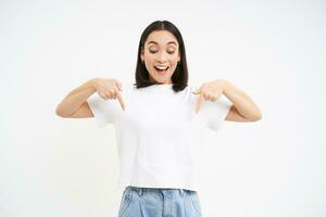 retrato de hermosa sonriente coreano chica, puntos dedos abajo, muestra anuncio publicitario, demuestra bandera abajo, aislado en blanco antecedentes foto