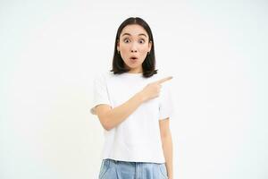 retrato de niña con sorprendido rostro, señalando dedo Derecha a promoción bandera, asombrado por anuncio publicitario, blanco antecedentes foto