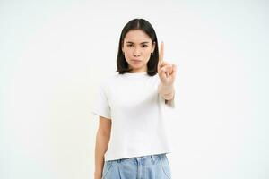 Serious 25 years woman, shows one finger, stop sign, warning gesture, disapprove smth, stands over white background photo