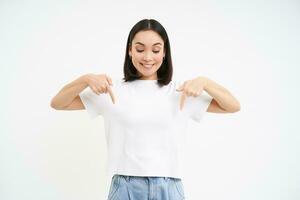 Portrait of beautiful smiling korean girl, points fingers down, shows advertisement, demonstrates banner below, isolated on white background photo