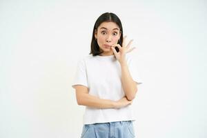 Asian woman hears gossips and zips her mouth, seal lips to keep promise, stands over white background photo