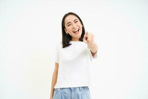 entusiasta asiático mujer, puntos dedo a cámara, felicitando, echar un vistazo tú, atractivo gente, aislado en blanco antecedentes foto