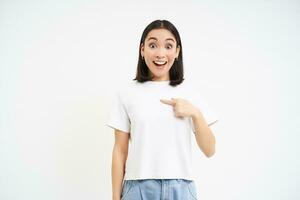 entusiasta joven mujer, puntos a sí misma con sorprendido sonriente rostro, siendo elegido, trabajar como voluntario, en pie terminado blanco antecedentes foto