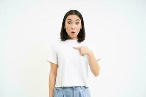 Portrait of female model, pointing finger at herself with confused face, being mentioned, isolated on white background photo