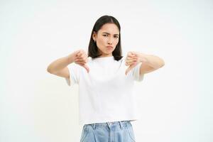 Upset young woman shows thumbs down, dislike, isolated on white background photo