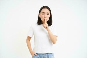 Portrait of girl shushes, shhh gesture, speaks silently, taboo to say something, tells secret, stands over white background photo