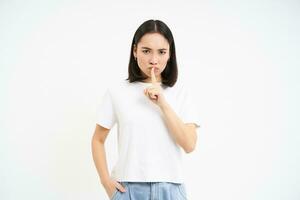 Portrait of girl shushes, shhh gesture, speaks silently, taboo to say something, tells secret, stands over white background photo