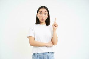 Eureka. Asian woman raises one finger, has suggestion, got an idea, pointing up, isolated against white background photo