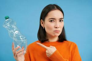 retrato de mujer señalando a el plastico botella con grave rostro, azul antecedentes foto