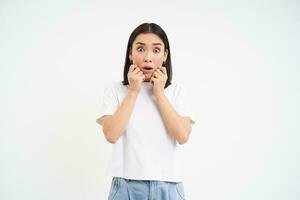 Portrait of shocked, scared asian woman, gasping and jumping scared, white background photo