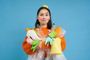 Environment and ecology. Portrait of asian woman holding plastic waste, pile of garbage, blue background photo