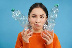 Thinking angry girl, shows two bottles, recycling plastic, goes green, reusable trash, blue background photo