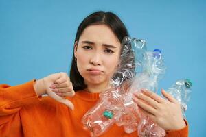 retrato de mujer con trastornado rostro, muestra pulgar abajo y el plastico botellas, decepcionado con carencia de reciclaje, azul antecedentes foto