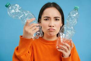 retrato de triste asiático mujer con el plastico botellas, trastornado por carencia de reciclaje centros, azul antecedentes foto