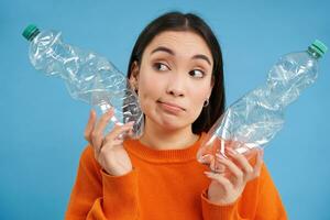 Girl with two plastic bottles, thinking and looking aside, sorting trash, saving planet by recycling, blue background photo