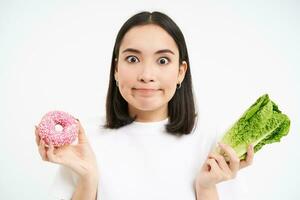 Healthy clean detox eating concept. Vegetarian, vegan, raw concept. Asian woman holds cabbage vegetable and unhealthy tasty doughnut, white background photo