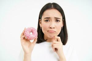 cerca arriba de triste linda chica, muestra sabroso vidriado rosquilla, siendo en dieta, hipocresía tratar delicioso rosquilla, basura comida concepto foto