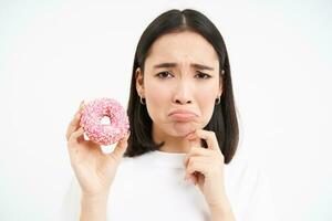 Close up of sad cute girl, shows tasty glazed doughnut, being on diet, cant try delicious donnut, junk food concept photo