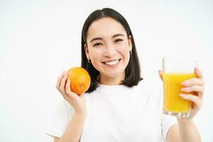 cerca arriba de sonriente morena chica, bebidas Fresco jugo, sostiene naranja fruta, blanco estudio antecedentes foto