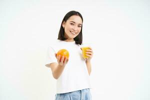 sano sonriente coreano chica, bebidas Fresco jugo exprimido desde naranjas, corsé saludable, tiene normal dieta, blanco antecedentes foto