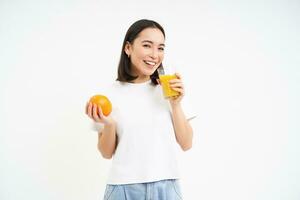 sano sonriente coreano chica, bebidas Fresco jugo exprimido desde naranjas, corsé saludable, tiene normal dieta, blanco antecedentes foto