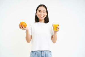 hermosa y sano joven mujer, empieza su día con Fresco jugo, participación naranja Fruta y sonriente, blanco antecedentes foto