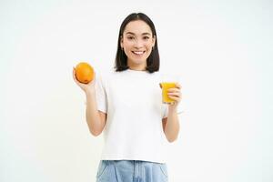 sonriente coreano mujer sostiene naranja joder y jugo, concepto de bienestar y sano nutrición, blanco antecedentes foto