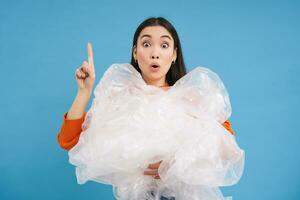 Asian female eco-activist, woman looks surprised, holds plastic waste, preserving nature, standing over blue background photo