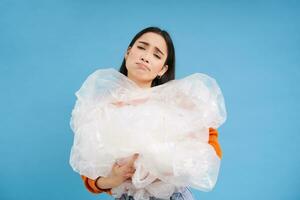 asiático triste mujer participación el plastico basura y ceñudo desde decepción, luchando contaminación, eco-activista clasificación desperdiciar, azul antecedentes foto