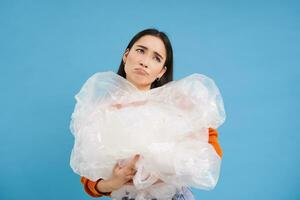 Asian sad woman holding plastic garbage and frowning from disappointment, fighting polution, eco-activist sorting waste, blue background photo