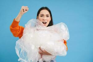 Angry eco-activist holding plastic waste, raising fist and fighting for environment, sorting garbage, recycling, blue background photo