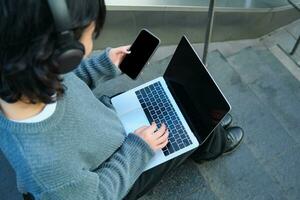 Close up portrait of girl, student works on laptop and listens music in headphones. Blank computer screen and hands typing on keyboard photo