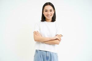 joven entusiasta coreano mujer, mira con confianza, soportes en poder actitud y sonrisas, blanco antecedentes foto
