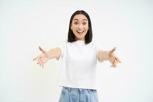 Friendly smiling asian woman, reaching her hands towards camera, hugging, welcoming you, standing over white background photo