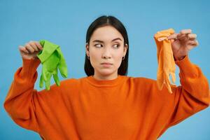Image of girl with bothered face, showing two dirty cleaning gloves, found garbage, looking disappointed, blue background photo
