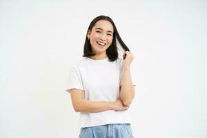 joven entusiasta coreano mujer, mira con confianza, soportes en poder actitud y sonrisas, blanco antecedentes foto