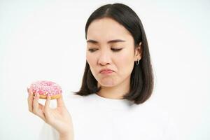 Close up of sad cute girl, shows tasty glazed doughnut, being on diet, cant try delicious donnut, junk food concept photo