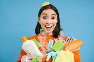 retrato de entusiasta coreano mujer, participación vacío el plastico botellas, clasificación basura, sonriente y mirando feliz, aislado en azul antecedentes foto